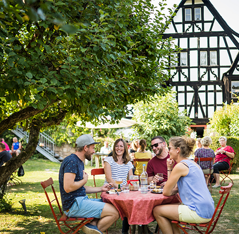 Freunde sitzen zusammen am Tisch und essen Zwiebelkuchen und trinken Federweisser